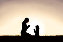 Mother Praying With Her Young Child Outside At Sunset.