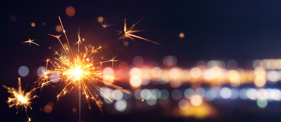 Glittering burning sparkler against blurred bokeh light background