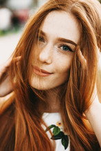 Close Up Portrait Of A Amazing Red Haired Girl With Freckles And Green Eyes Looking At Camera Smiling Touching Her Red Hair Outside.