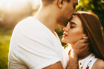 Wall Mural - Amazing close up portrait of a lovely red hair girl with freckles with closed eyes kissed by her boyfriend on the forehead against sunset while traveling.