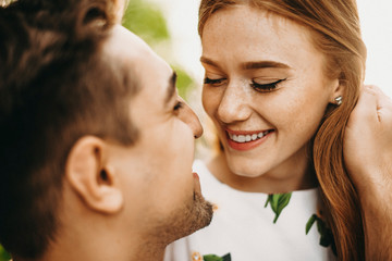 Close up portrait of a beautiful young couple where red hair girl with freckles trying to kiss her boyfriend smiling touching her red hair.