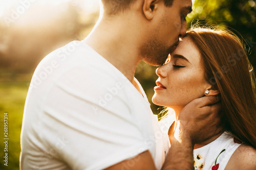 Amazing close up portrait of a lovely red hair girl with freckles with closed eyes kissed by her boyfriend on the forehead against sunset while traveling Tableau sur Toile
