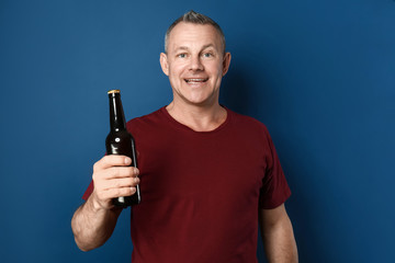 Wall Mural - Happy middle-aged man with bottle of beer on color background