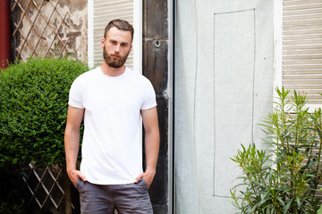 Wall Mural - Hipster handsome male model with beard wearing white blank t-shirt with space for your logo or design in casual urban style