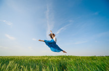 Flying Dancer In The Air. Happy Woman Ballerina In Blue Fabric Skirt Making A Big Jump On Green Field. Summer Or Spring Concept 