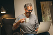 © cherryandbees - middle aged man using laptop and drinking tea relaxed in his sofa at home