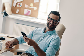 Canvas Print - Cheerful businessman. Young modern businessman looking at camera and smiling while sitting in the office