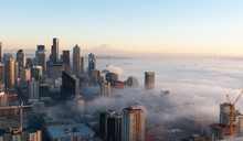 Partially Immersed In The Fog From Elliott Bay, This Panoramic View Of Seattle At Sunset,in A Cold Autumn Day, With Blue Sky And The Mount Rainier Visible On The Background.