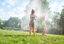 Sister And Brother Playing With Watering Hose In Hot Summer Afternoon On  Family Country House Grass Yard.