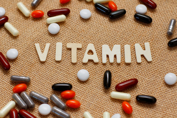 Vitamin concept text by wooden letters on brown rough fabric texture.  Set of different pills.