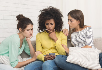 Upset girl looking at phone, friends calming her