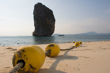 Close-up Yellow Buoys With Rope  On The Beach ,The Background Image Is A Rocky Island And The Sea