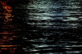 Fototapeta Kwiaty - Blurred light reflection on river surface with water waves in the dark night 