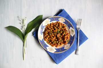 Canvas Print - chickpea with meat made in red sauce served in white and blue plate with fork and lily of the valley flower