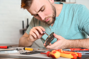 Wall Mural - Technician repairing mobile phone at table in workshop, closeup