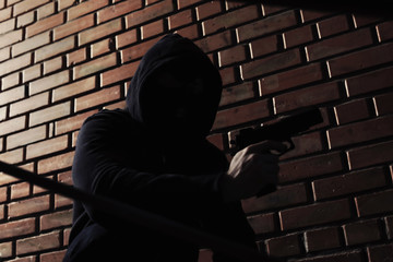Wall Mural - Man in hoodie with gun indoors. Dangerous criminal