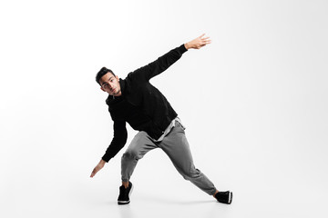 Wall Mural - Stylish young man is dancing hip-poh on a white background. He is bending his knees and spreading his arms to the sides