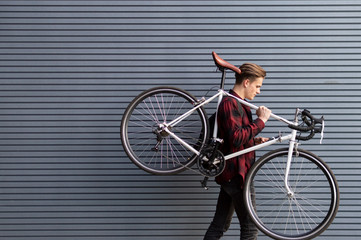 young handsome guy carries a broken bike on his shoulders against the wall, the student goes on foot