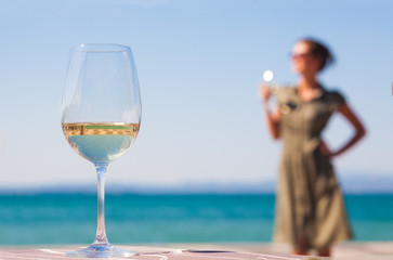 Wall Mural - glass of red wine on table over young woman Lazise backgound