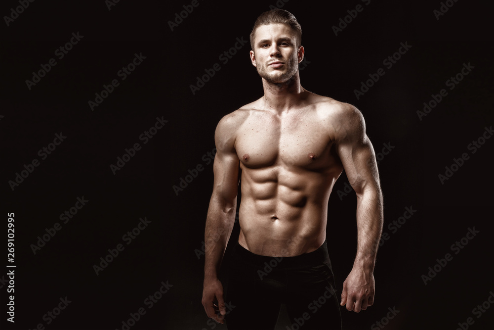 Muscular model young man on dark background. Fashion portrait of strong brutal guy with trendy hairstyle. Sexy naked torso, six pack abs. Male flexing his muscles. Sport workout bodybuilding concept. - obrazy, fototapety, plakaty 