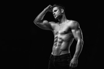 Wall Mural - Muscular model young man on dark background. Black and white fashion portrait of strong brutal guy with modern trendy hairstyle. Sexy naked torso six pack abs. Male flexing his muscles. Sport concept.