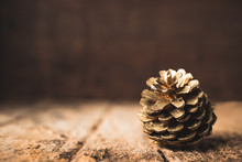 Gold Pine Cone On Grunge Wood Table And Dark Brown Wooden Wall.Winter Merry Christmas Holiday Greeting Card
