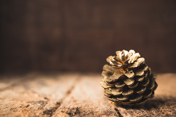 Poster - gold pine cone on grunge wood table and dark brown wooden wall.Winter Merry Christmas holiday greeting card