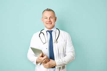 Wall Mural - Handsome middle-aged doctor with tablet PC on color background