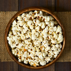 Homemade fresh savory popcorn with cheese, garlic and dried oregano in wooden bowl, photographed overhead on dark wood with natural light (Selective Focus, Focus on the top of the popcorn)