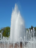 Fototapeta Tęcza - City fountain: jets and voluminous sparkling splashes against the blue summer sky