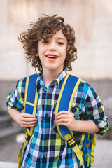 Cute Schoolboy going to school. Portrait of a 7 years old guy with his backpack in a windy day. Children going back to school concept.