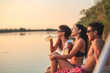 © BalanceFormCreative - Group of friends sitting and having fun on the pier by the lake on sunset.
