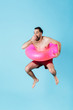 Photo of joyful shirtless tourist man wearing rubber ring smiling while swimming and jumping