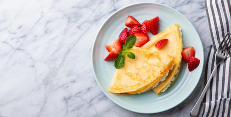 Wall Mural - Crepes, thin pancakes with cream cheese, ricotta and fresh strawberries. Marble background. Top view. Copy space.