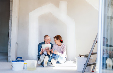 Poster - Senior couple painting walls in new home, using tablet. Relocation concept.