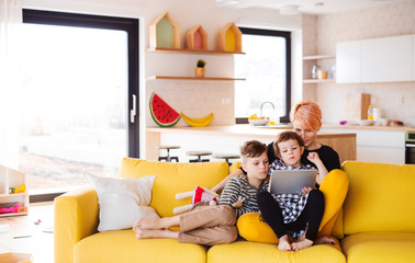 A young woman with two children indoors at home, using tablet.