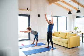 Sticker - A senior couple indoors at home, doing exercise in living room.