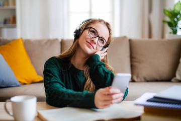 Poster - A young female student sitting at the table, using headphones when studying.