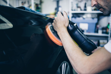 Car detailing - Hands with orbital polisher in auto repair shop. Selective focus.