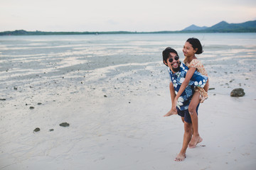 The daughter rides behind the father for a walk on the beach.