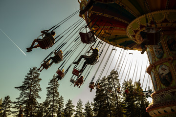 Kouvola, Finland - 18 May 2019: Ride Swing Carousel in motion in amusement park Tykkimaki and aircraft trail in sky.