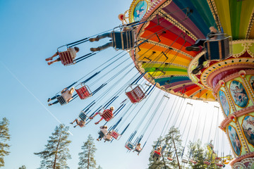 Kouvola, Finland - 18 May 2019: Ride Swing Carousel in motion in amusement park Tykkimaki and aircraft trail in sky.