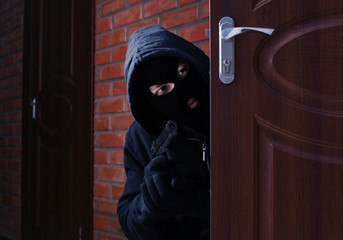 Wall Mural - Masked man with gun spying behind open door indoors. Criminal offence