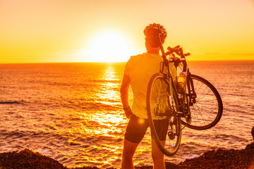 triathlon road bike cyclist carrying bicycle watching sunset after outdoor race training by ocean co