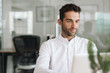 © mavoimages - Smiling young businessman working on a laptop at his desk