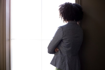 Silhouette of a stressed out black African American businesswoman looking worried and thinking about problems and failure by the office window.  She looks depressed or upset about debt or bankruptcy.