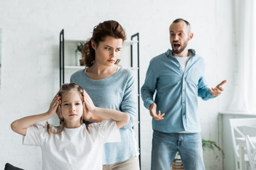 selective focus of mother covering ears on daughter while man screaming at home