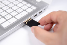 Human Hand Plugging In An SD Media Card Into The Personal Laptop Computer On White Background.