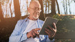 © VAKSMANV - Close up portrait of senior man with a beard smiling while standing outside in sunlight.