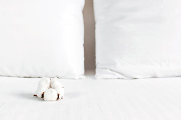 Soft white quilted pillow and cotton flower in bed on the background of white leather quilted headboard. Clean pillow, part of bed close-up, comfort. Quilted headboard background, bedding mockup